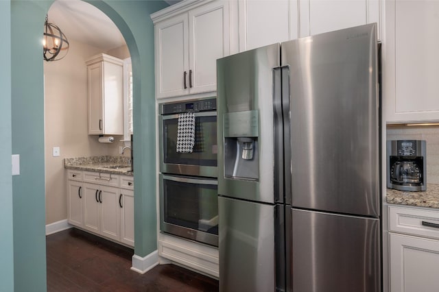 kitchen featuring appliances with stainless steel finishes, dark wood-style flooring, arched walkways, a sink, and baseboards