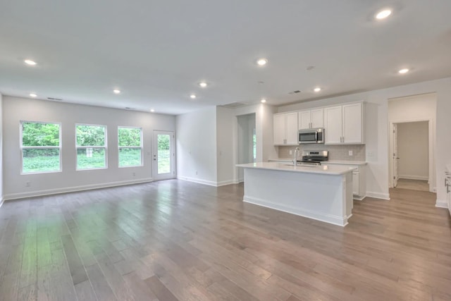kitchen featuring appliances with stainless steel finishes, open floor plan, light countertops, light wood-type flooring, and an island with sink