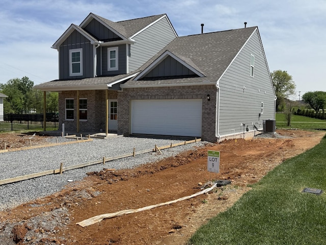 view of front of house with board and batten siding, central AC, driveway, brick siding, and roof with shingles