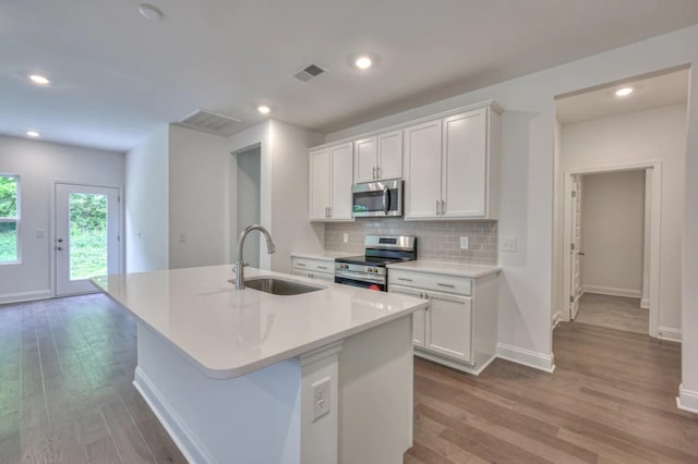 kitchen with stainless steel appliances, a sink, wood finished floors, an island with sink, and backsplash