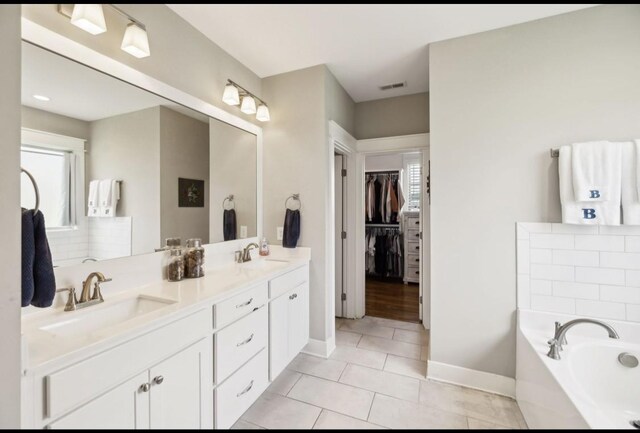 full bath featuring tile patterned flooring, a garden tub, baseboards, a walk in closet, and double vanity