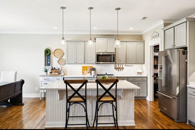 kitchen featuring stainless steel appliances, crown molding, decorative backsplash, a breakfast bar area, and gray cabinetry