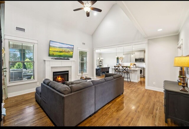 living room with ceiling fan, a lit fireplace, high vaulted ceiling, wood finished floors, and baseboards