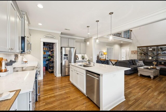 kitchen with appliances with stainless steel finishes, a sink, ornamental molding, light countertops, and decorative light fixtures