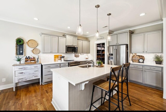 kitchen with appliances with stainless steel finishes, gray cabinetry, crown molding, decorative backsplash, and a breakfast bar
