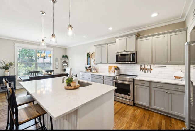 kitchen featuring stainless steel appliances, gray cabinets, a sink, crown molding, and a kitchen bar