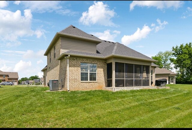 rear view of property featuring central air condition unit, brick siding, a sunroom, and a yard