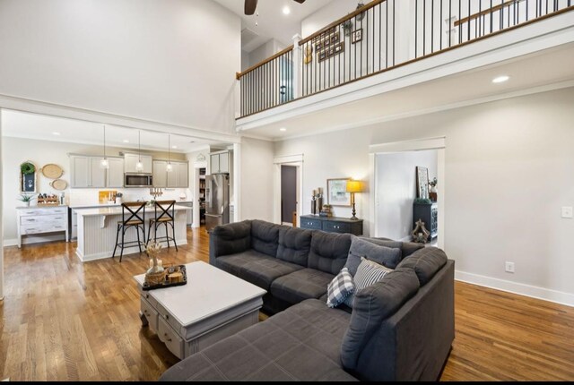 living area featuring a towering ceiling, baseboards, ceiling fan, light wood-style flooring, and recessed lighting