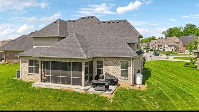 rear view of house featuring brick siding, a patio, a sunroom, and a lawn