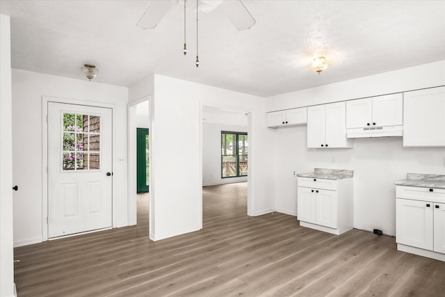 kitchen with light wood finished floors, under cabinet range hood, a ceiling fan, white cabinets, and light countertops