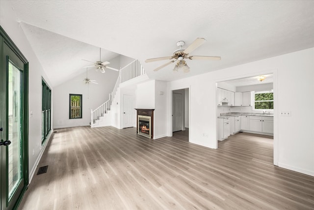 unfurnished living room featuring ceiling fan, light wood-type flooring, baseboards, a glass covered fireplace, and a textured ceiling