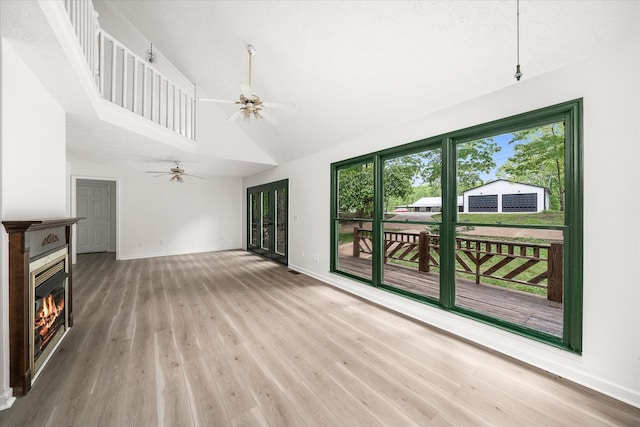 unfurnished living room featuring a glass covered fireplace, a ceiling fan, light wood finished floors, baseboards, and high vaulted ceiling