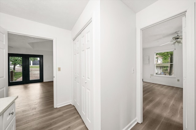 hallway with light wood finished floors, baseboards, and french doors