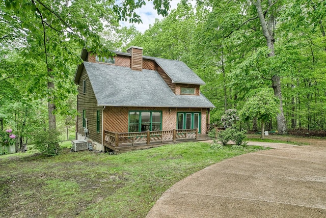 rustic home with a shingled roof, a chimney, central air condition unit, a wooden deck, and a front lawn