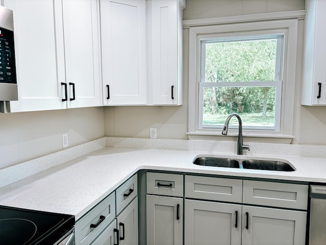 kitchen with a sink, appliances with stainless steel finishes, gray cabinetry, light stone countertops, and white cabinets