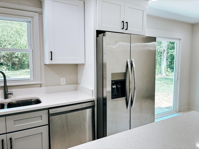 kitchen featuring appliances with stainless steel finishes, a sink, light stone counters, and white cabinetry