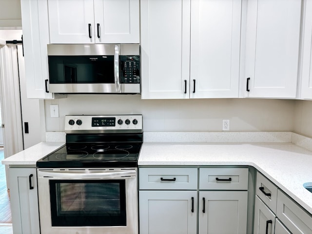 kitchen featuring stainless steel appliances, white cabinets, and light stone countertops