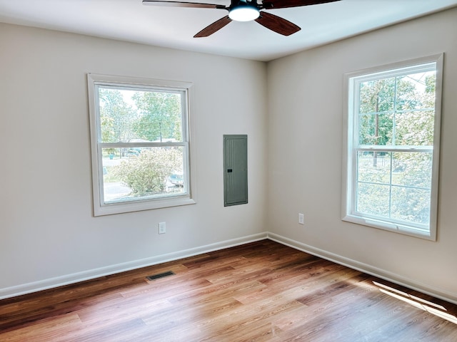 unfurnished room featuring electric panel, healthy amount of natural light, wood finished floors, and a ceiling fan