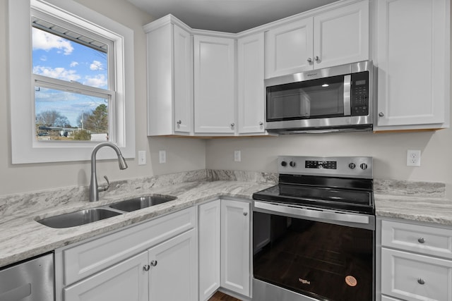 kitchen featuring stainless steel appliances, a sink, white cabinets, and light stone countertops