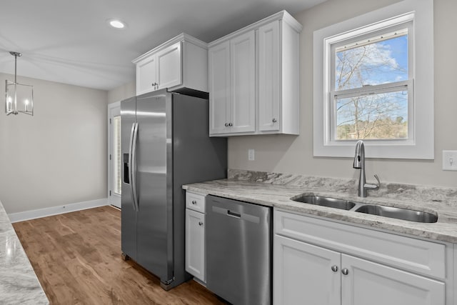 kitchen with appliances with stainless steel finishes, a sink, white cabinetry, wood finished floors, and a chandelier