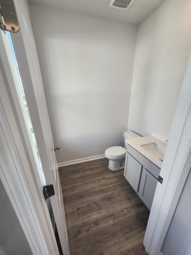 half bath with wood finished floors, toilet, and vanity
