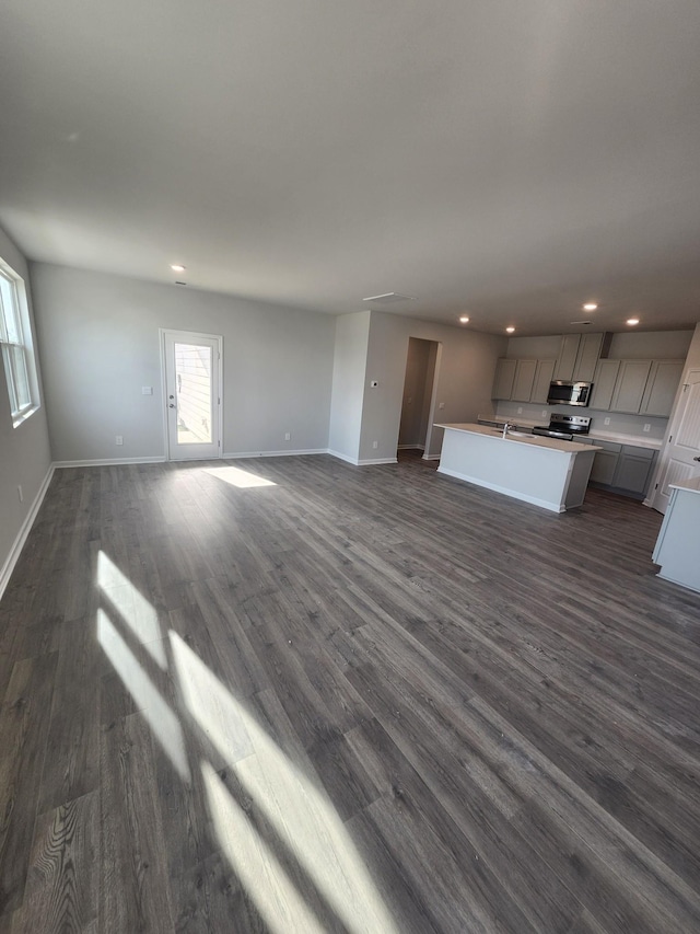 unfurnished living room with recessed lighting, dark wood-type flooring, baseboards, and a sink