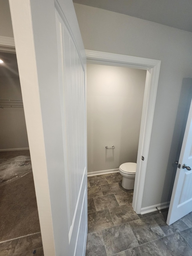 bathroom featuring toilet, baseboards, and stone finish flooring
