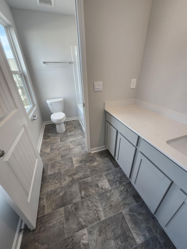 bathroom featuring stone finish floors, toilet, baseboards, and vanity