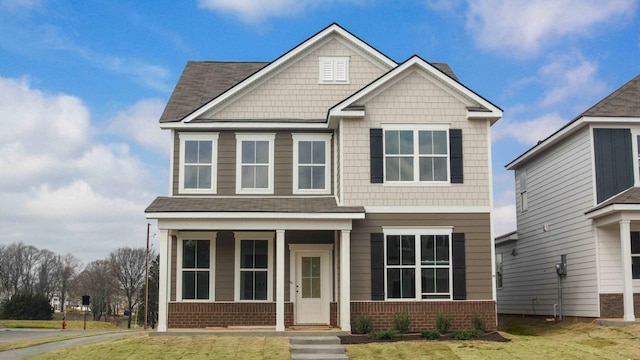 craftsman house featuring brick siding, a porch, a front lawn, and roof with shingles