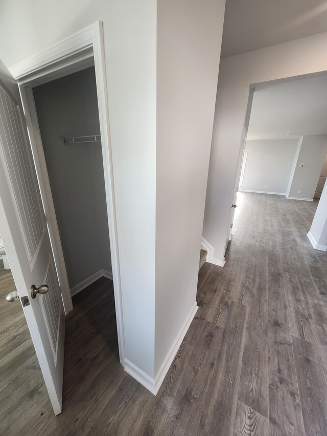 hall featuring dark wood-style flooring, baseboards, and an upstairs landing