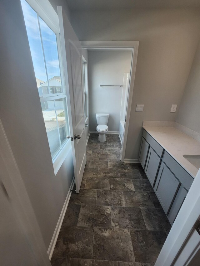 bathroom with stone finish floors, toilet, baseboards, and vanity