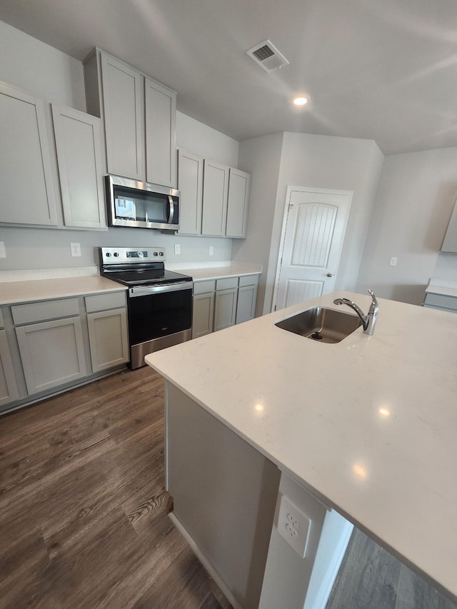 kitchen with stainless steel appliances, a sink, light countertops, dark wood-style flooring, and gray cabinetry