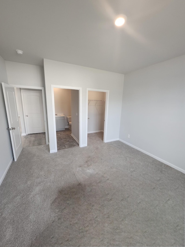unfurnished bedroom featuring carpet flooring, baseboards, a walk in closet, connected bathroom, and a closet
