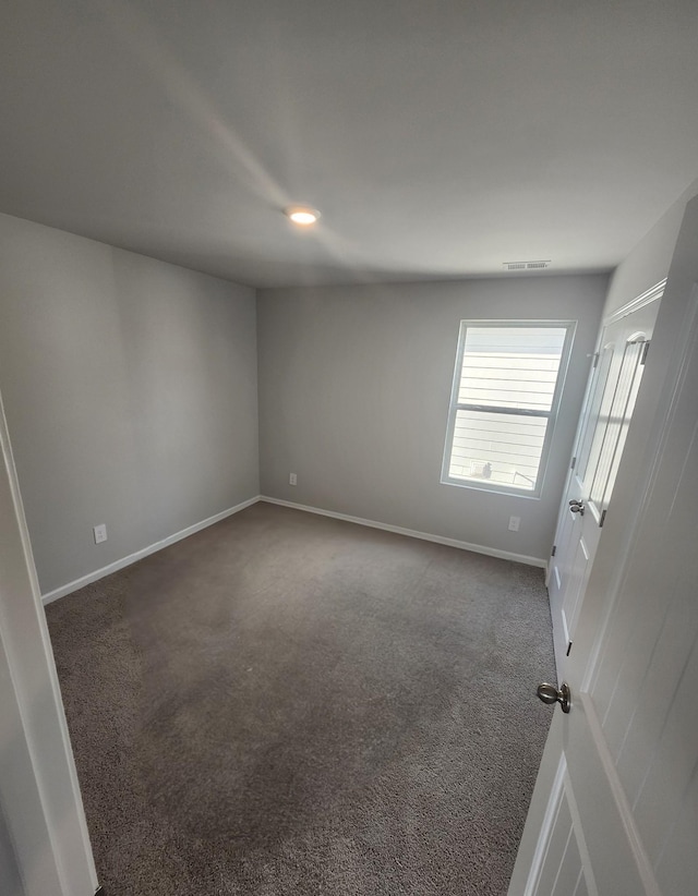 unfurnished room featuring dark colored carpet and baseboards