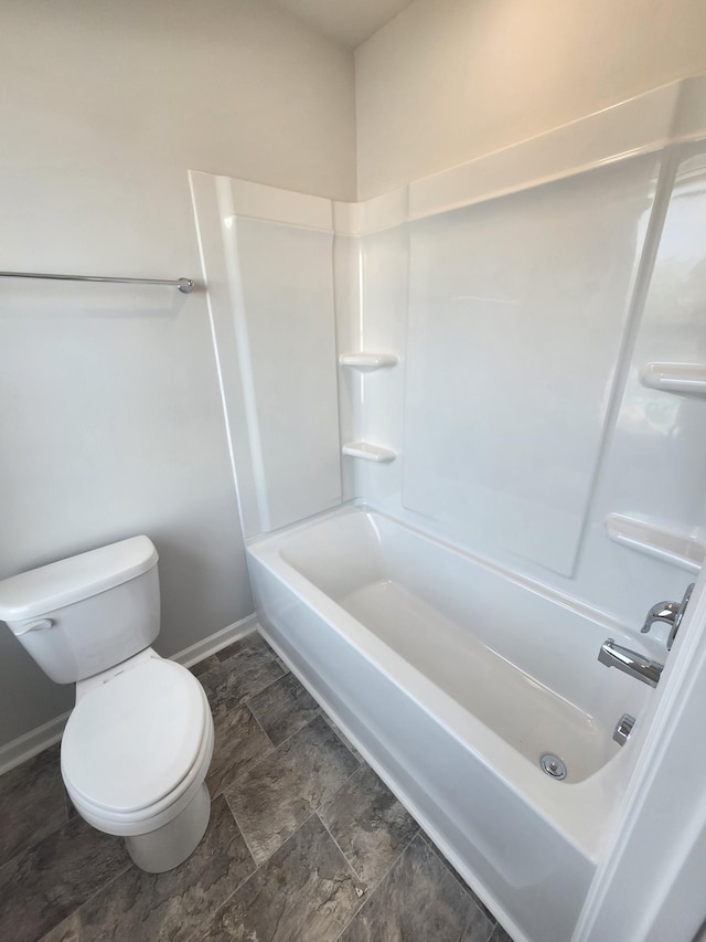 full bathroom with baseboards, toilet,  shower combination, and stone finish floors