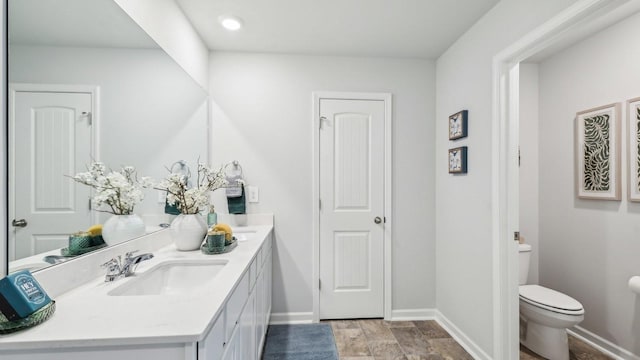 bathroom with toilet, double vanity, and baseboards