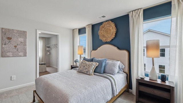 bedroom featuring carpet flooring, baseboards, multiple windows, and a walk in closet