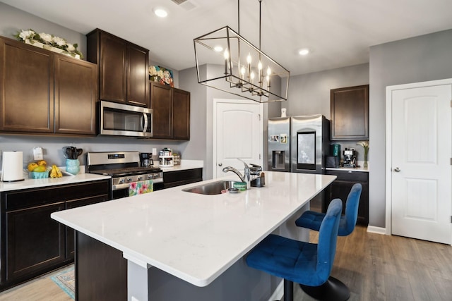7401 Brady Ln, Antioch, TN 37013 - kitchen featuring appliances with stainless steel finishes, a sink, a breakfast bar, light wood finished floors, and dark brown cabinetry