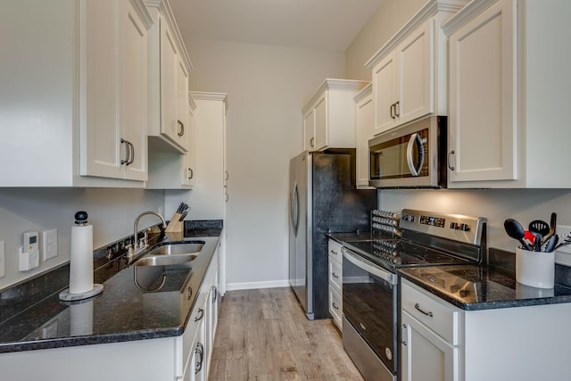 kitchen featuring stainless steel appliances, a sink, light wood-style floors, white cabinetry, and dark stone countertops