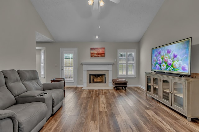 living area with lofted ceiling, a ceiling fan, healthy amount of natural light, wood finished floors, and a fireplace