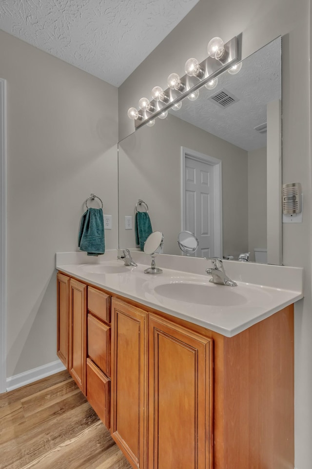 bathroom with a textured ceiling, wood finished floors, double vanity, and toilet