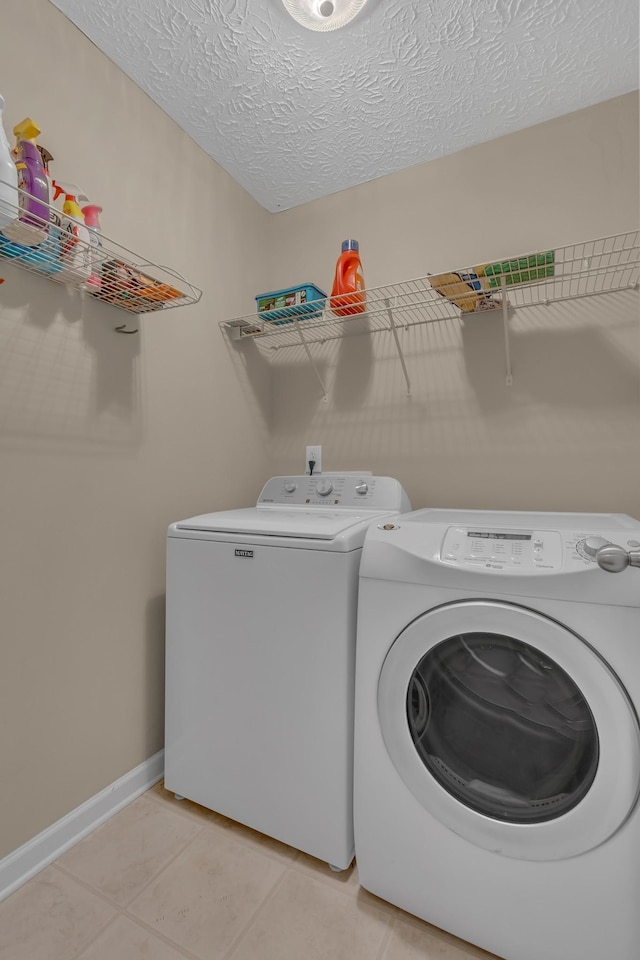 clothes washing area with washer and dryer, light tile patterned flooring, baseboards, and a textured ceiling