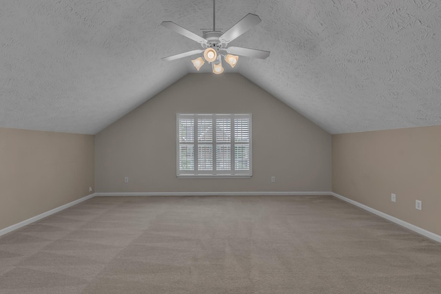 additional living space featuring a textured ceiling, carpet, baseboards, a ceiling fan, and vaulted ceiling
