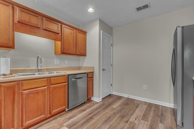 kitchen with stainless steel appliances, a sink, light wood finished floors, brown cabinets, and light countertops