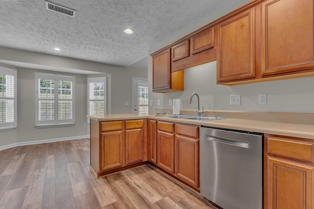 kitchen with stainless steel dishwasher, a sink, brown cabinetry, light countertops, and a peninsula