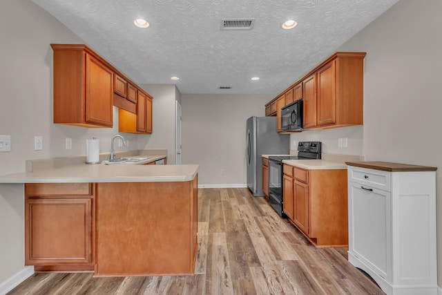 kitchen with black appliances, a sink, a textured ceiling, light wood-type flooring, and light countertops