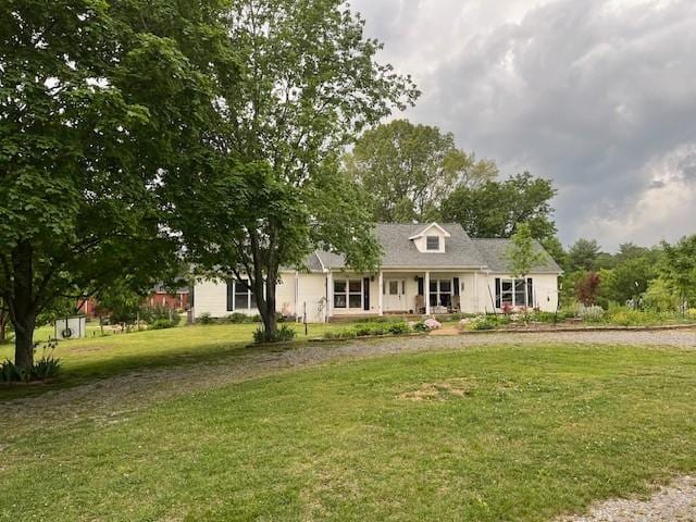 new england style home featuring covered porch, a front lawn, and curved driveway