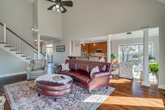 living area with decorative columns, wood finished floors, ceiling fan, plenty of natural light, and a high ceiling