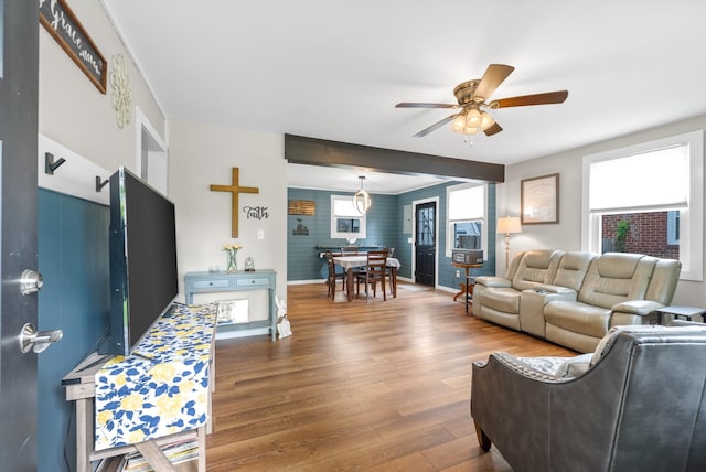 living room featuring a ceiling fan, wood finished floors, baseboards, and an accent wall