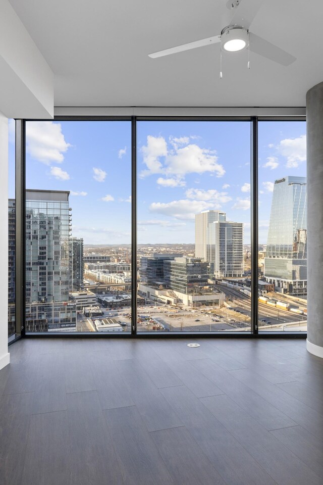 empty room with expansive windows, a view of city, wood finished floors, and ceiling fan